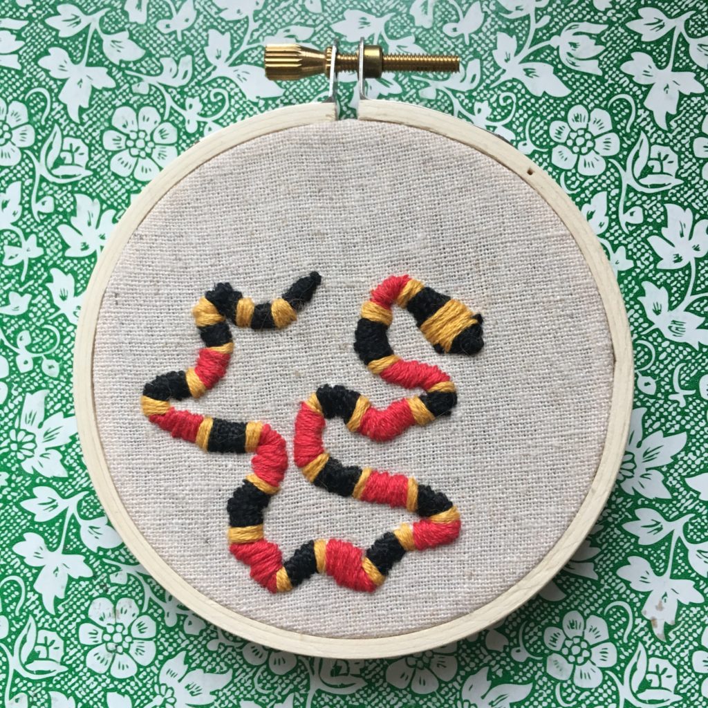 an embroidery of a coral snake on beige linen