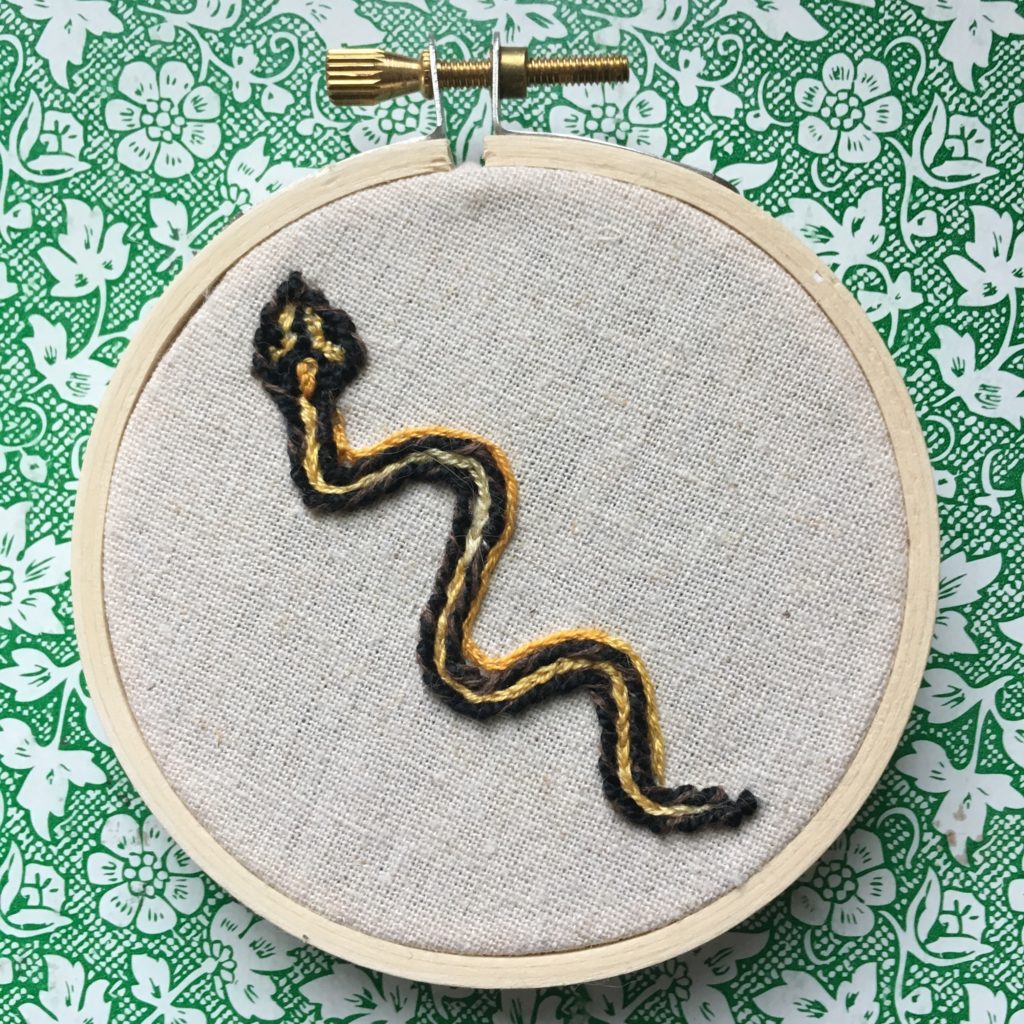 an embroidery of a garter snake on beige linen
